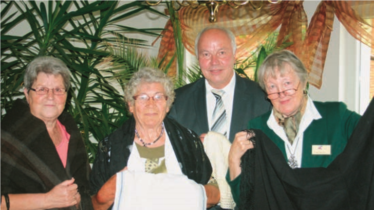 &Uuml;bergabe von bessarabischen Kleidungsst&uuml;- cken an den Bessarabiendeutschen Verein durch Frau Jortzig. V.l.n.r.: Wilma Gaier (verantwortlich f&uuml;r die Veranstaltung vor Ort in M&ouml;ckern), Frau Jortzig, Wolfgang Bunk (Moderation der Veranstaltung) und Erika Wiener (stellvertretende Bundesvor- sitzende, Organisation der Veranstaltung)